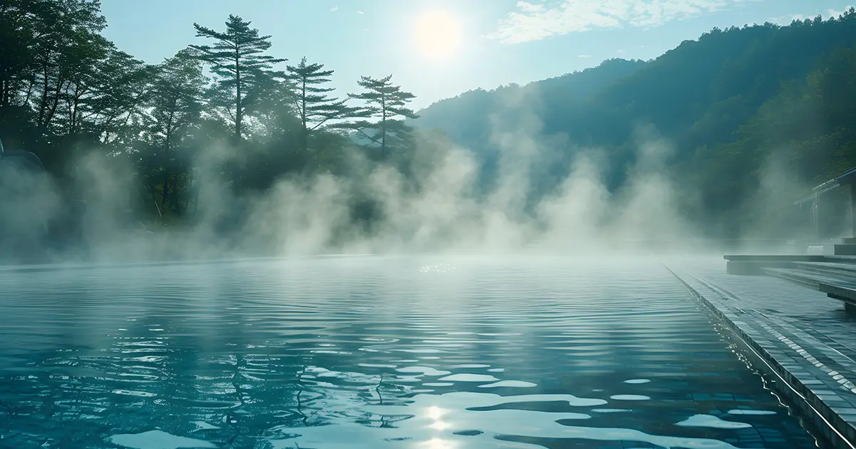 Piscina externa com água quente emitindo vapor ao ar livre perto da natureza. Imagem de destaque do artigo da GDA sobre os principais acessórios para aquecer piscina com economia e evitar a perda de calor.
