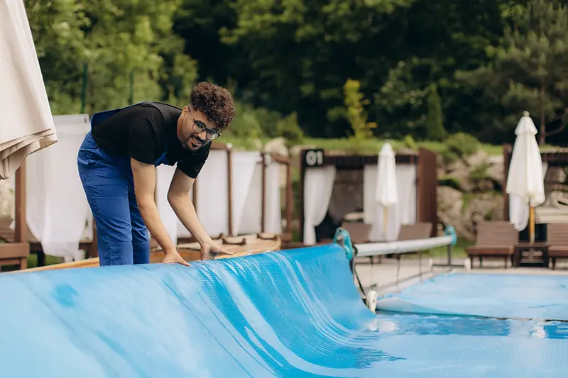 Exemplo de capa térmica bolha azul instalada sobre a água de uma piscina moderna, vista de um ambiente interno com grandes janelas de vidro. Componente indispensável para a retenção de calor e eficiência no aquecimento de piscina.