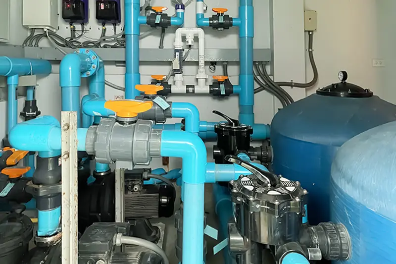 Vista interna detalhada de uma casa de máquinas da piscina com tubulações azuis, registros, bombas e filtros instalados.