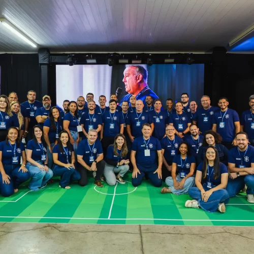 Foto em grupo da equipe GDA Indústria reunida na 5ª Convenção de Vendas, todos vestindo camisas azuis com a logo da marca em um ambiente de evento corporativo.